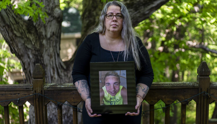 A portrait of a mother standing outside, holding a picture of her late son.
